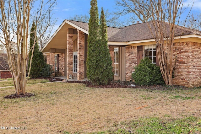 view of front of house featuring a shingled roof, a front lawn, and brick siding