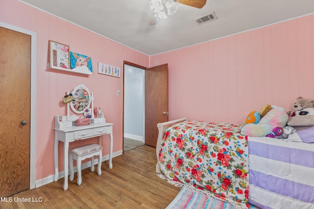 bedroom featuring hardwood / wood-style floors, ceiling fan, and wooden walls