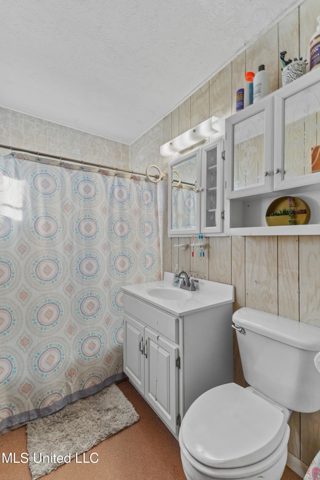 bathroom with vanity, toilet, a textured ceiling, and wooden walls