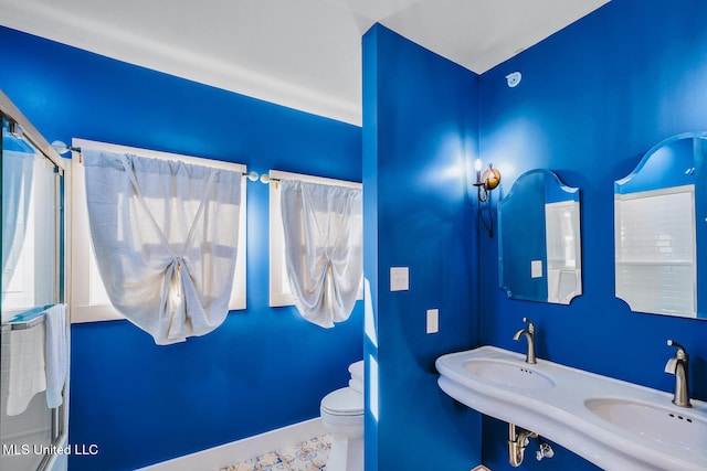 bathroom featuring dual sinks, a shower with shower door, and toilet