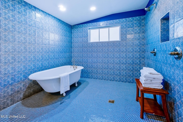 bathroom with tile patterned flooring, vaulted ceiling, tile walls, and a tub