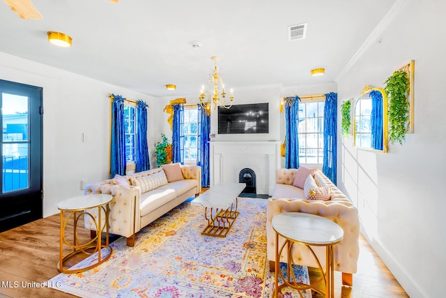 living room featuring light wood-type flooring, an inviting chandelier, crown molding, and a healthy amount of sunlight