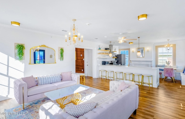 living room with ceiling fan with notable chandelier, ornamental molding, sink, and light hardwood / wood-style flooring