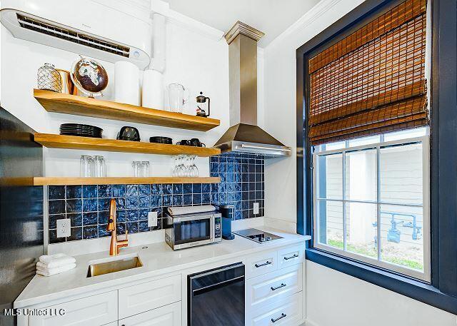 kitchen featuring black electric stovetop, backsplash, sink, wall chimney range hood, and white cabinetry