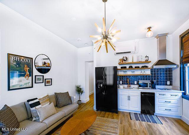 bar with black appliances, wall chimney exhaust hood, white cabinets, and backsplash