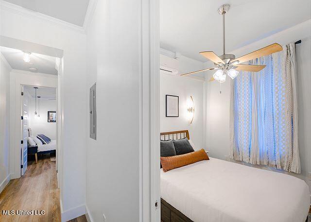 bedroom featuring ceiling fan, a wall mounted air conditioner, electric panel, light hardwood / wood-style floors, and ornamental molding