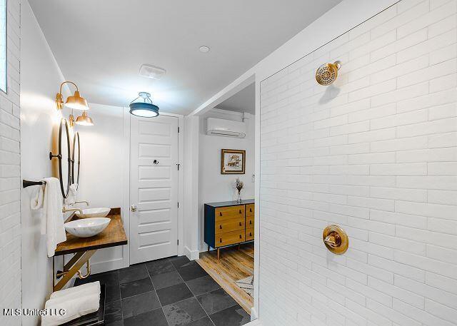 bathroom featuring a wall unit AC, hardwood / wood-style floors, brick wall, and sink