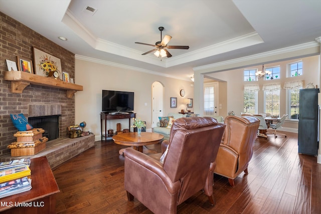 living room with ornamental molding, a brick fireplace, dark hardwood / wood-style floors, and a tray ceiling