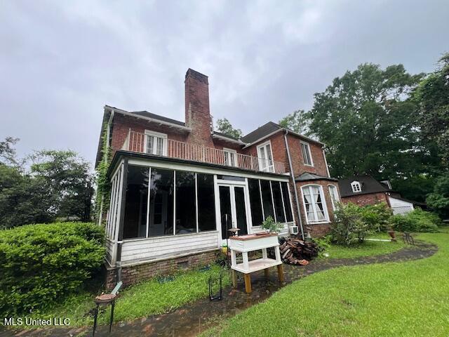 back of house with a sunroom, a yard, a chimney, and a balcony