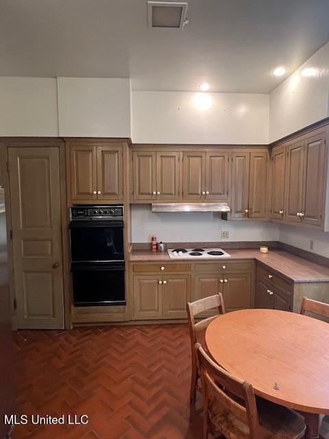 kitchen featuring brick floor, under cabinet range hood, light countertops, dobule oven black, and white stovetop