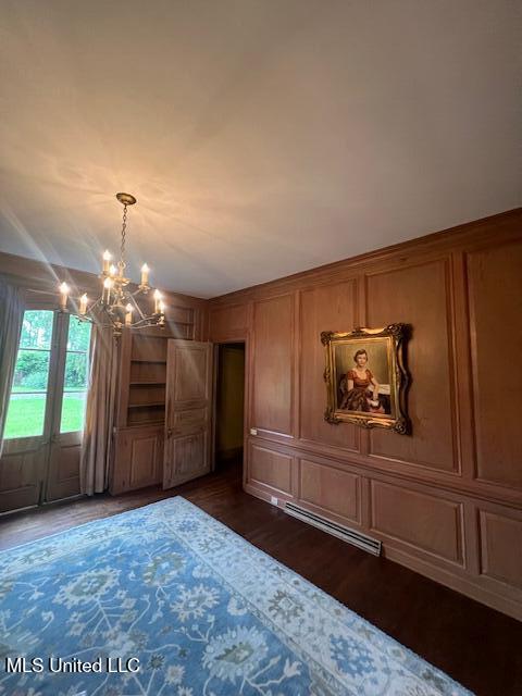 unfurnished bedroom with dark wood-style floors, a notable chandelier, a decorative wall, and a baseboard radiator