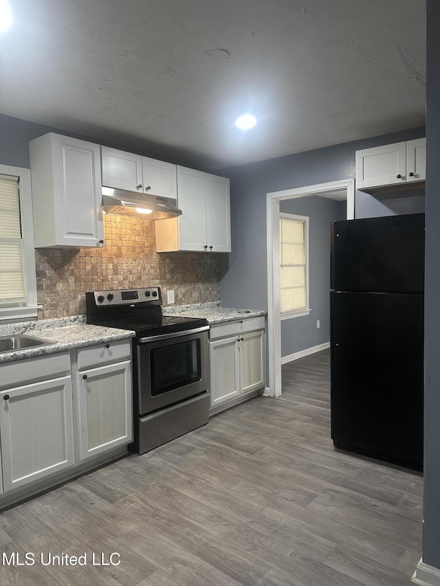 kitchen featuring white cabinets, stainless steel electric range oven, freestanding refrigerator, tasteful backsplash, and under cabinet range hood