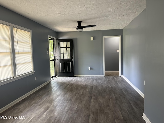 empty room featuring dark wood-type flooring, a ceiling fan, a textured ceiling, and baseboards