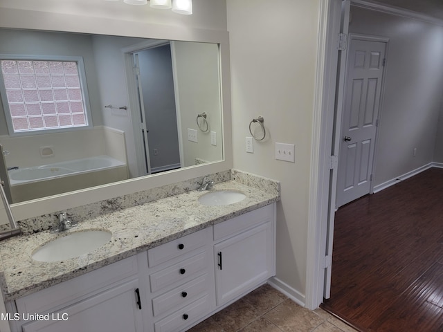 full bathroom with double vanity, a bath, baseboards, and a sink