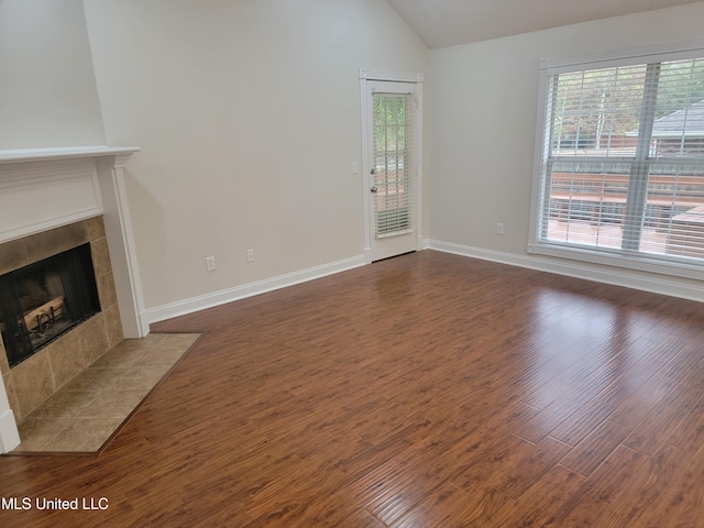 unfurnished living room featuring baseboards, wood finished floors, a tiled fireplace, and vaulted ceiling