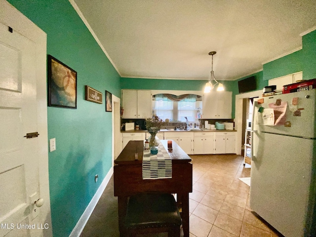 kitchen featuring white cabinets, crown molding, decorative light fixtures, light tile patterned floors, and freestanding refrigerator