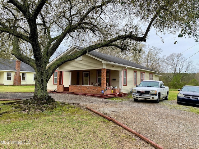 view of front of house with gravel driveway, a porch, and a front yard