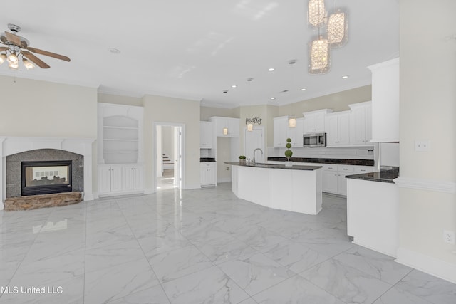 kitchen featuring a center island with sink, crown molding, hanging light fixtures, built in shelves, and white cabinetry