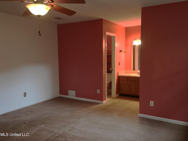 unfurnished bedroom with ceiling fan, a walk in closet, ensuite bathroom, and light carpet