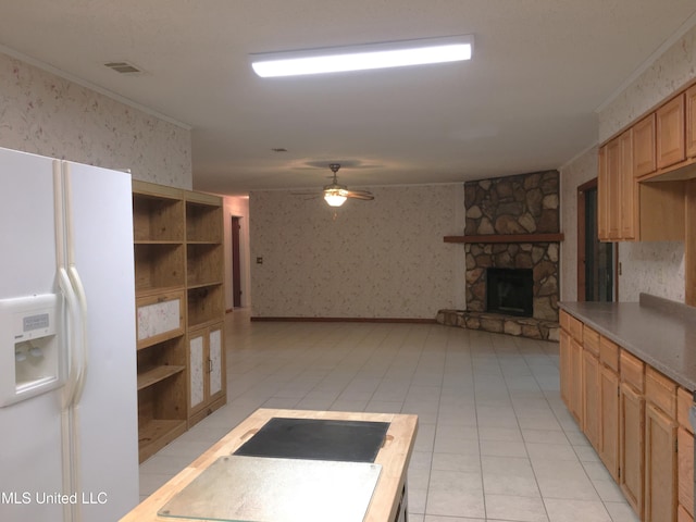 kitchen with white refrigerator with ice dispenser, crown molding, ceiling fan, light tile patterned floors, and a fireplace