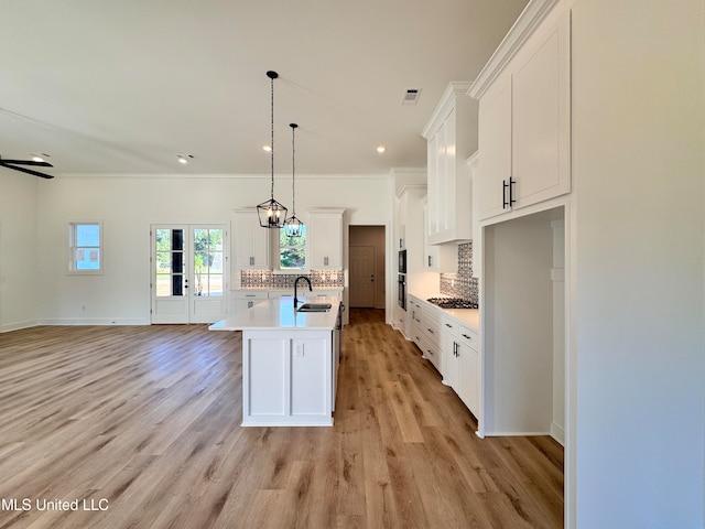 kitchen featuring stainless steel gas cooktop, decorative light fixtures, white cabinets, light hardwood / wood-style flooring, and a kitchen island with sink