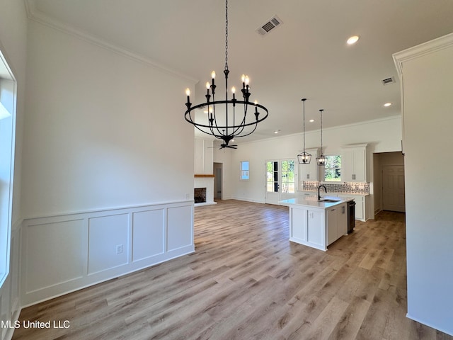 kitchen with a kitchen island with sink, sink, hanging light fixtures, and light wood-type flooring