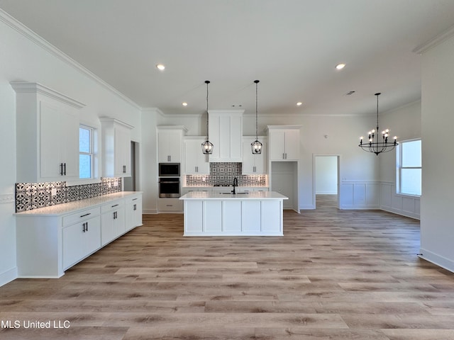 kitchen with sink, a kitchen island with sink, white cabinetry, and light wood-type flooring