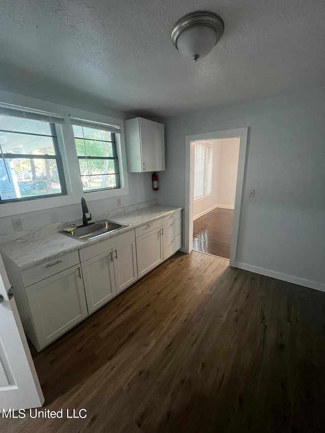 kitchen featuring white cabinetry, light stone countertops, a textured ceiling, dark wood-type flooring, and sink