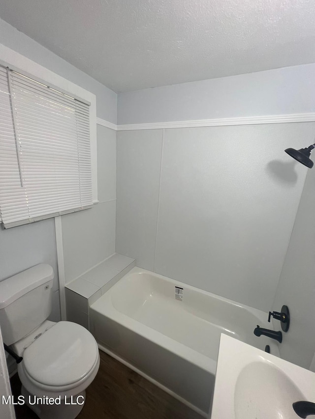 bathroom featuring toilet, hardwood / wood-style floors, a textured ceiling, and a bath