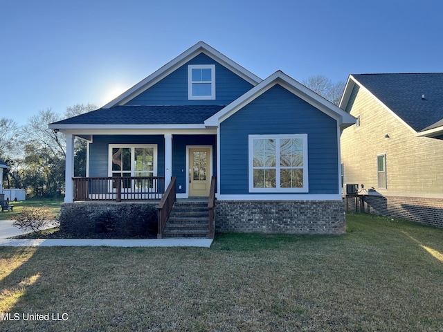 bungalow with a shingled roof, covered porch, a front lawn, and central AC unit