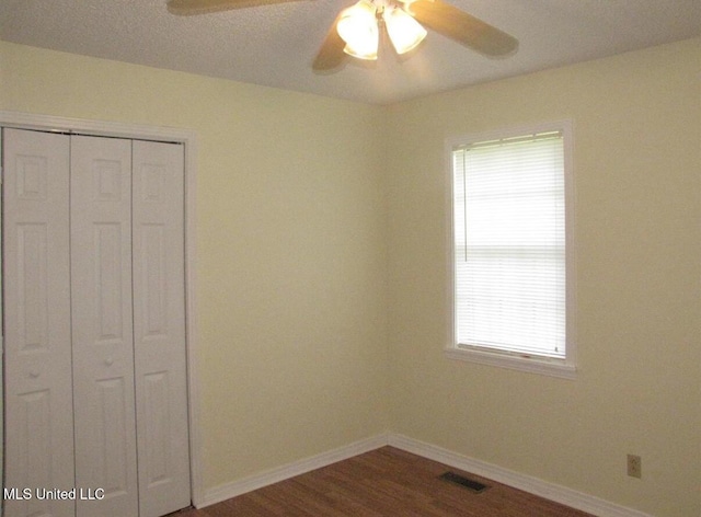 unfurnished bedroom featuring a closet, baseboards, dark wood finished floors, and ceiling fan
