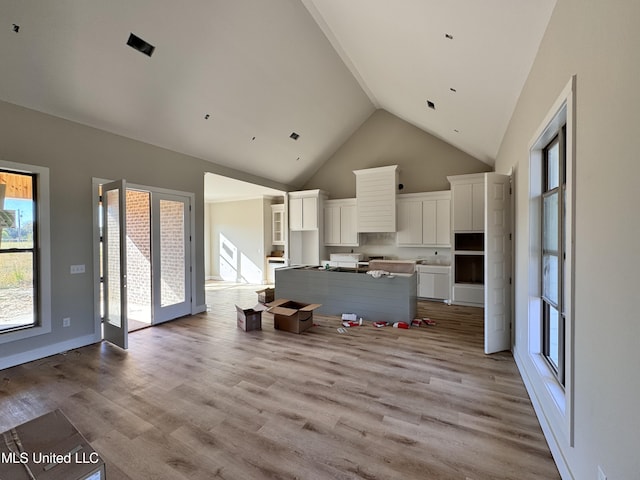 kitchen featuring white cabinetry, a kitchen island, light wood-type flooring, and high vaulted ceiling