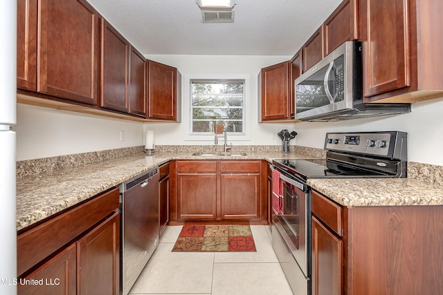 kitchen featuring sink, light tile patterned floors, appliances with stainless steel finishes, light stone counters, and a textured ceiling