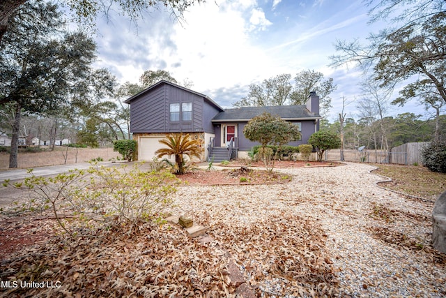 split level home featuring concrete driveway, fence, a chimney, and an attached garage