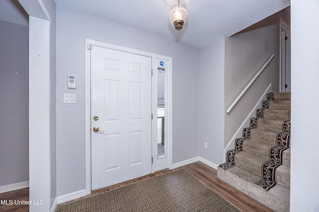 foyer entrance featuring dark wood-style flooring, a textured ceiling, baseboards, and stairs