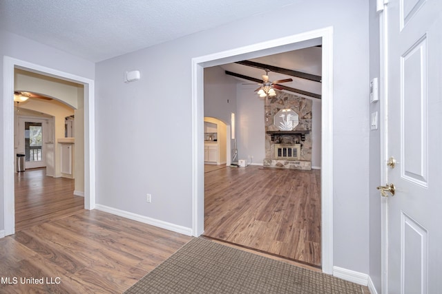 corridor with arched walkways, a textured ceiling, wood finished floors, and baseboards