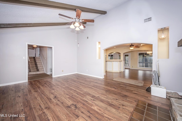 unfurnished living room featuring arched walkways, beam ceiling, dark wood-type flooring, and visible vents