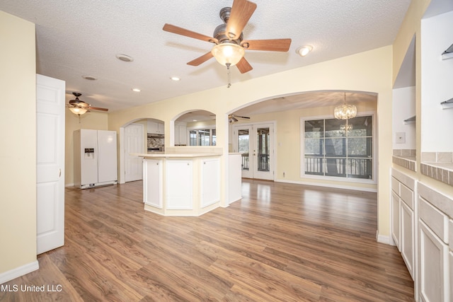 kitchen with dark wood-style floors, white refrigerator with ice dispenser, light countertops, hanging light fixtures, and open floor plan