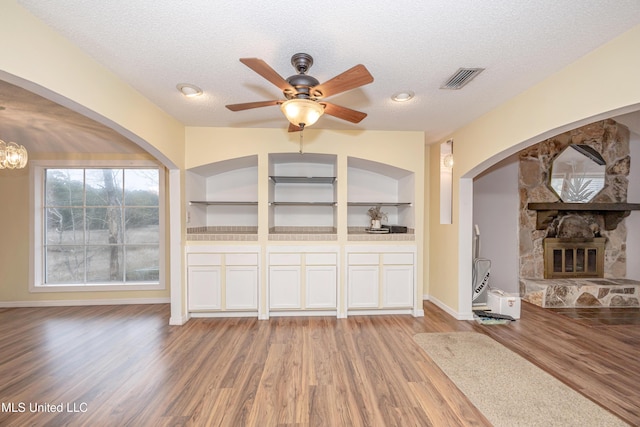 unfurnished living room with light wood-style flooring, visible vents, a stone fireplace, and a textured ceiling