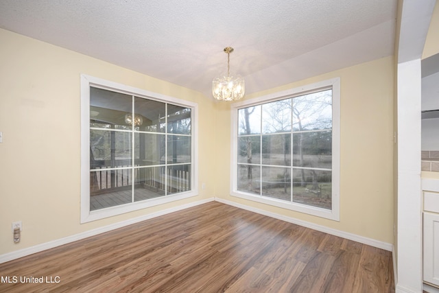 unfurnished dining area with an inviting chandelier, a textured ceiling, baseboards, and wood finished floors