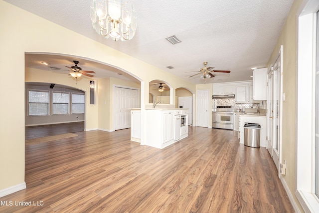 kitchen with stainless steel range, a kitchen island, open floor plan, hanging light fixtures, and white cabinetry