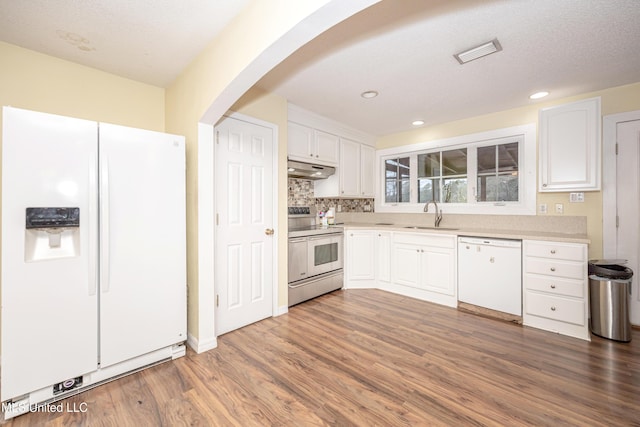 kitchen with arched walkways, light countertops, white cabinets, a sink, and white appliances