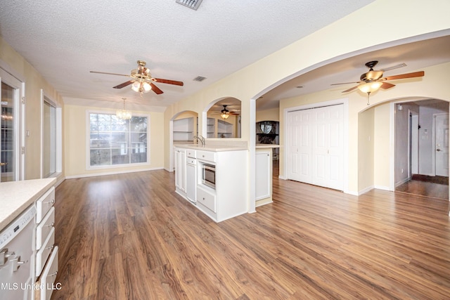 kitchen featuring arched walkways, stainless steel microwave, dark wood-style flooring, light countertops, and white cabinetry