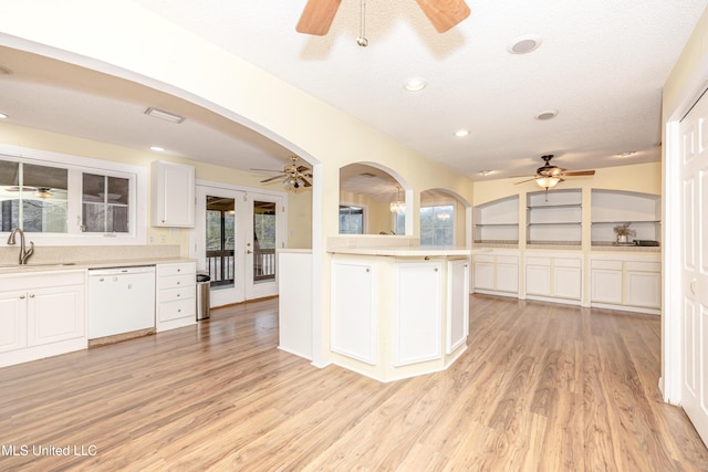 kitchen with white cabinets, white dishwasher, light countertops, and a sink