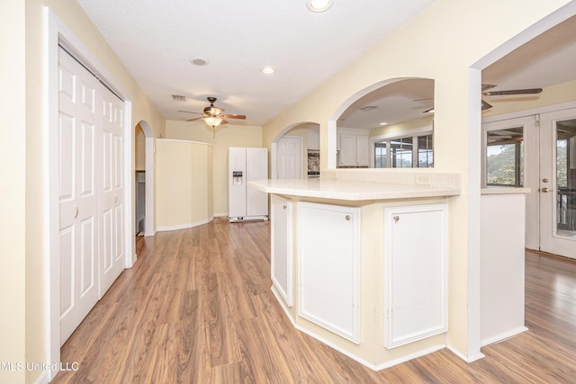 kitchen featuring a peninsula, white refrigerator with ice dispenser, a ceiling fan, light countertops, and light wood-type flooring