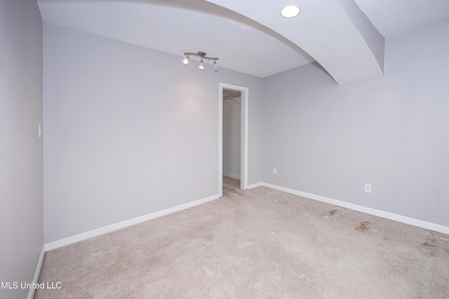 unfurnished room with arched walkways, light colored carpet, and baseboards