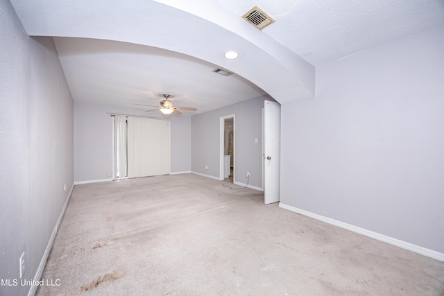 unfurnished room featuring light carpet, visible vents, arched walkways, a ceiling fan, and baseboards