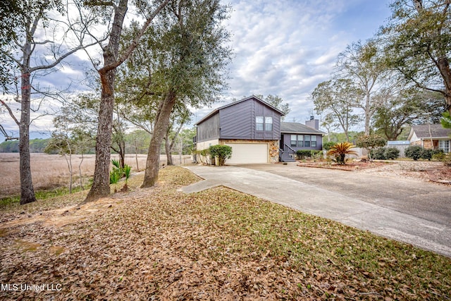 view of side of property featuring a garage, stone siding, a chimney, and concrete driveway