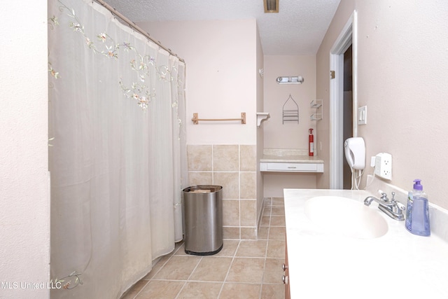 bathroom with a textured ceiling, tile patterned flooring, vanity, visible vents, and tile walls