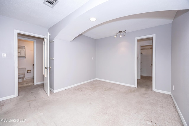 spare room featuring light carpet, baseboards, visible vents, arched walkways, and a textured ceiling